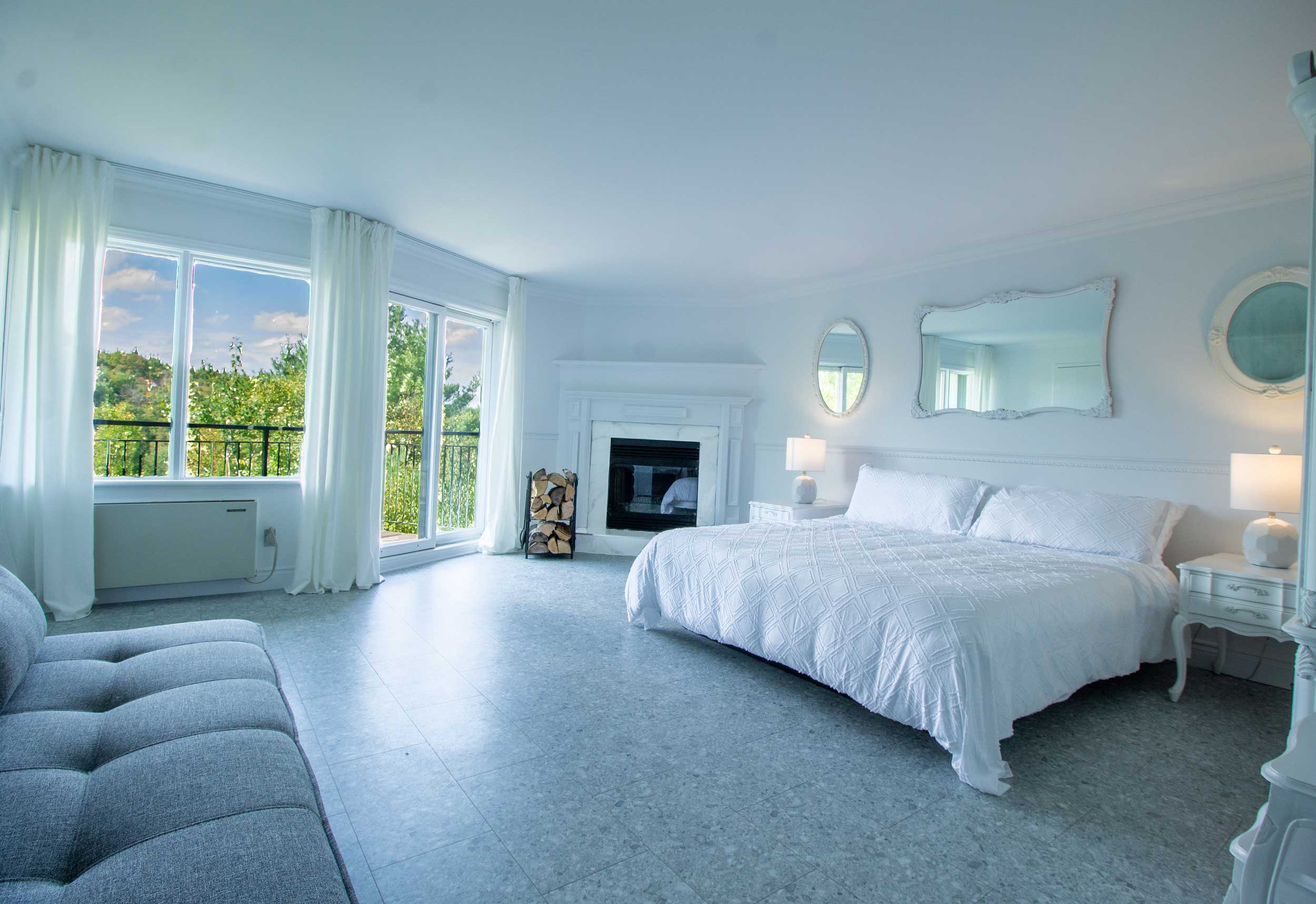 grande chambre blanche avec balcon lit et divan auberge domaine du lac long lanaudiere